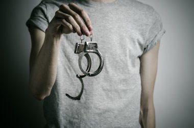 Hapishane ve hüküm giymiş Konu: adam elinde kelepçe tecavüzcü koymak Studio, gri bir arka plan üzerinde gri bir T-shirt üzerinde kelepçe ile
