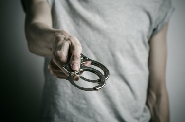 Prison and convicted topic: man with handcuffs on his hands in a gray T-shirt on a gray background in the studio, put handcuffs on rapist clipart