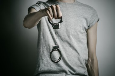 Prison and convicted topic: man with handcuffs on his hands in a gray T-shirt on a gray background in the studio, put handcuffs on rapist clipart