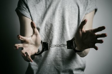 Hapishane ve hüküm giymiş Konu: adam elinde kelepçe tecavüzcü koymak Studio, gri bir arka plan üzerinde gri bir T-shirt üzerinde kelepçe ile