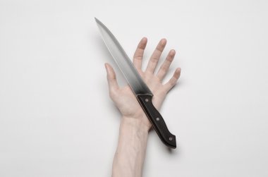 Murder and Halloween theme: A man's hand reaching for a knife, a human hand holding a knife isolated on a gray background in studio from above clipart