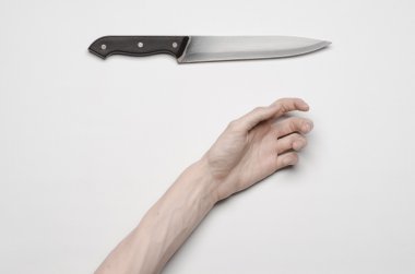 Murder and Halloween theme: A man's hand reaching for a knife, a human hand holding a knife isolated on a gray background in studio from above clipart