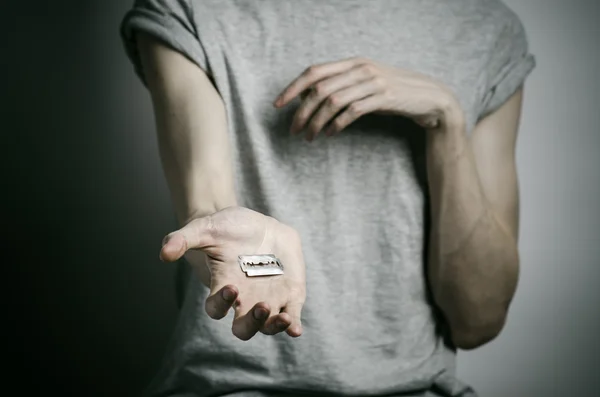 Depression and suicide theme: man holding a razor to suicide on a gray background in the studio — Stock Photo, Image