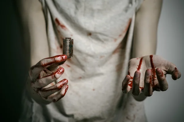 Depression and bloody Halloween theme: a man holding a bloody razor for suicide on a gray background in the studio — Stock Photo, Image