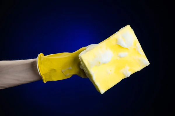Nettoyage de la maison et assainissement thème : Main tenant une éponge jaune mouillée avec de la mousse sur un fond bleu foncé en studio — Photo
