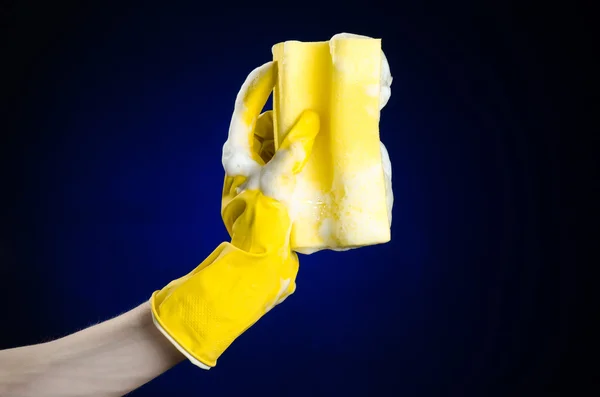 Pulizia della casa e igiene argomento: mano che tiene una spugna gialla bagnata con schiuma su uno sfondo blu scuro in studio — Foto Stock