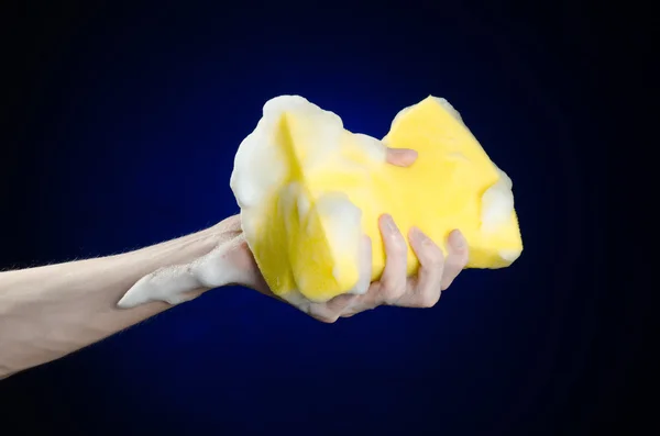 Cleaning the house and sanitation topic: Hand holding a yellow sponge wet with foam on a dark blue background in studio — Stock Photo, Image
