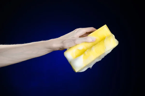 Limpeza da casa e tema de saneamento: Mão segurando uma esponja amarela molhada com espuma em um fundo azul escuro no estúdio — Fotografia de Stock