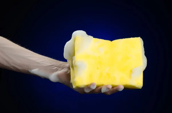 Καθαρισμός το σπίτι και την αποχέτευση θέμα: χέρι που κρατά ένα σφουγγάρι κίτρινο υγρό με αφρό σε σκούρο μπλε φόντο στο στούντιο — Φωτογραφία Αρχείου