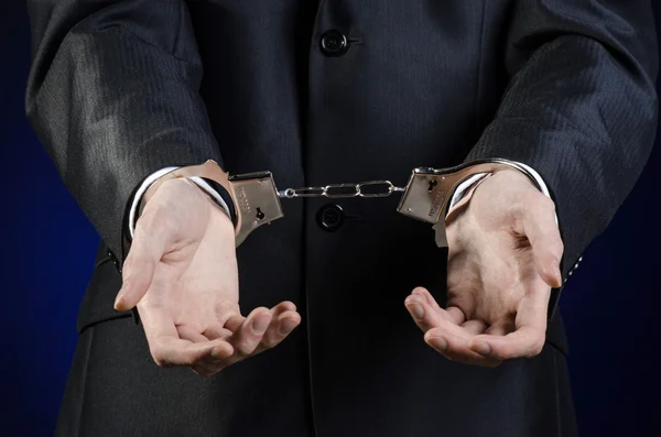 Corruption and bribery theme: businessman in a black suit with handcuffs on his hands on a dark blue background in studio isolated — Stock Photo, Image