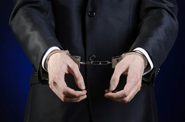 Коррупция и взяточничество тема: бизнесмен в черном костюме с наручниками на руках на темно-синем фоне в изолированной студии — стоковое фото