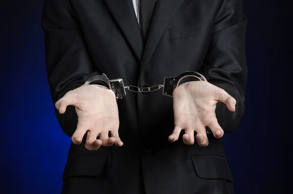 Korruption und Bestechung Thema: Geschäftsmann im schwarzen Anzug mit Handschellen an den Händen auf dunkelblauem Hintergrund im Studio isoliert — Stockfoto