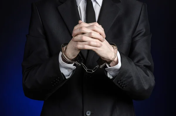 Corruptie en omkoping thema: zakenman in een zwart pak met handboeien op zijn handen op een donker blauwe achtergrond in studio geïsoleerd — Stockfoto