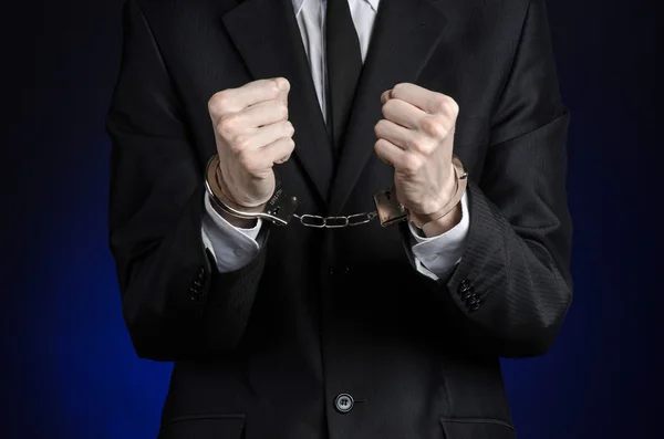 Corruption and bribery theme: businessman in a black suit with handcuffs on his hands on a dark blue background in studio isolated — Stock Photo, Image