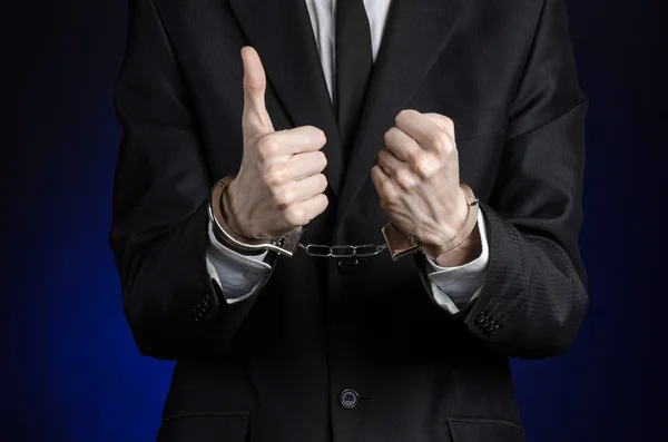 Corruption and bribery theme: businessman in a black suit with handcuffs on his hands on a dark blue background in studio isolated — Stock Photo, Image