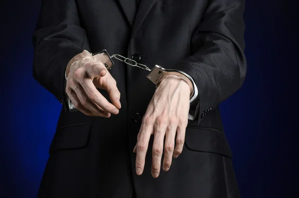 Corruption and bribery theme: businessman in a black suit with handcuffs on his hands on a dark blue background in studio isolated — Stock Photo, Image