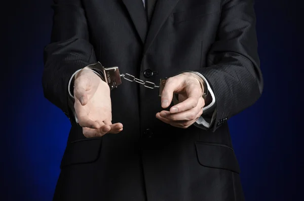 Corruption and bribery theme: businessman in a black suit with handcuffs on his hands on a dark blue background in studio isolated — Stock Photo, Image