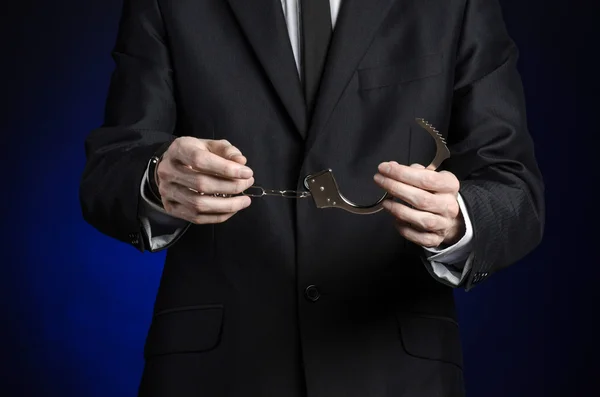 Corruption and bribery theme: businessman in a black suit with handcuffs on his hands on a dark blue background in studio isolated — Stock Photo, Image