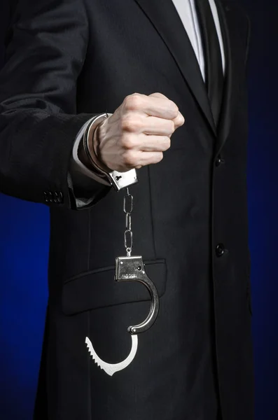 Corruption and bribery theme: businessman in a black suit with handcuffs on his hands on a dark blue background in studio isolated — Stock Photo, Image