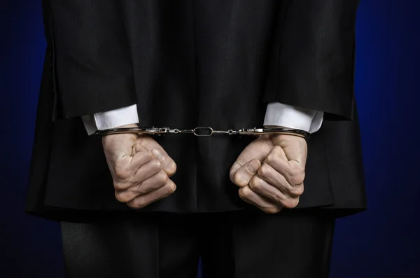 Corruption and bribery theme: businessman in a black suit with handcuffs on his hands on a dark blue background in studio isolated view from the back — Stock Photo, Image