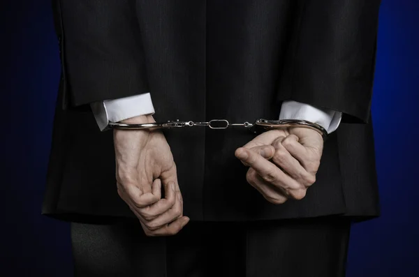 Korruption und Bestechung Thema: Geschäftsmann im schwarzen Anzug mit Handschellen an den Händen auf dunkelblauem Hintergrund im Studio isolierte Ansicht von hinten — Stockfoto