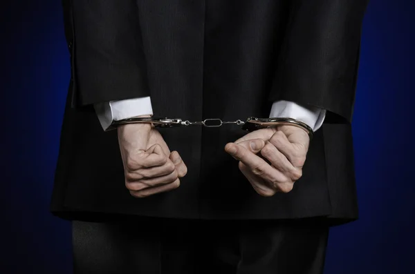 Corruption and bribery theme: businessman in a black suit with handcuffs on his hands on a dark blue background in studio isolated view from the back — Stock Photo, Image