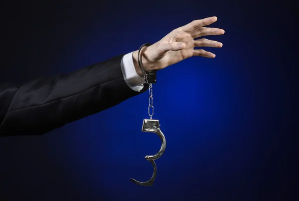 Corruption and bribery theme: businessman in a black suit with handcuffs on his hands on a dark blue background in studio isolated — Stock Photo, Image