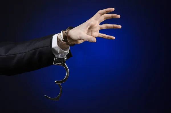 Corruption and bribery theme: businessman in a black suit with handcuffs on his hands on a dark blue background in studio isolated — Stock Photo, Image