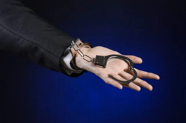 Διαφθορά και δωροδοκία θέμα: επιχειρηματίας σε ένα μαύρο κοστούμι με χειροπέδες στα χέρια του, σε σκούρο μπλε φόντο στο στούντιο απομονωθεί — Φωτογραφία Αρχείου