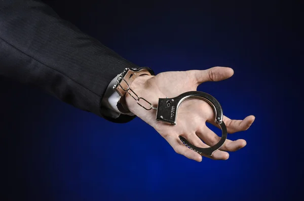 Corruption and bribery theme: businessman in a black suit with handcuffs on his hands on a dark blue background in studio isolated — Stock Photo, Image