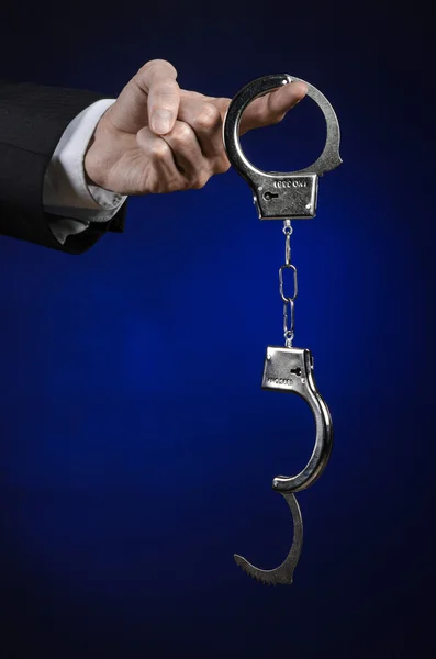 Corruption and bribery theme: businessman in a black suit with handcuffs on his hands on a dark blue background in studio isolated — Stock Photo, Image