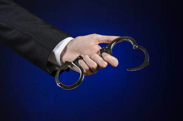 Διαφθορά και δωροδοκία θέμα: επιχειρηματίας σε ένα μαύρο κοστούμι με χειροπέδες στα χέρια του, σε σκούρο μπλε φόντο στο στούντιο απομονωθεί — Φωτογραφία Αρχείου