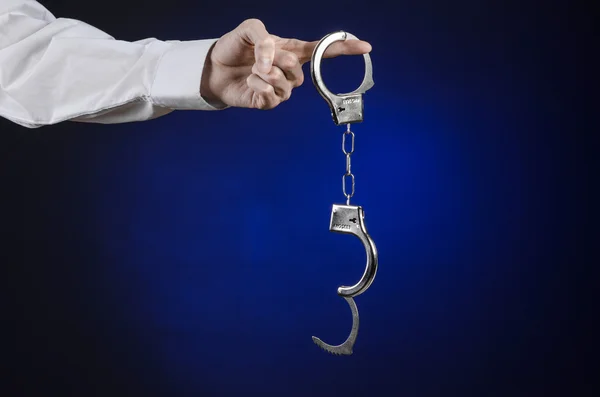 Nieuczciwi i temat lekarz więziennej: ręka mężczyzny w białej koszuli z kajdankami na ciemnym niebieskim tle w studio, umieścić kajdanki na lekarza, nielegalnej sprzedaży narządów — Zdjęcie stockowe