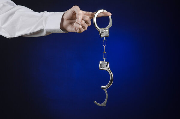 Dishonest and a prison doctor topic: the hand of man in a white shirt with handcuffs on a dark blue background in studio, put handcuffs on the doctor, the illegal sale of organs