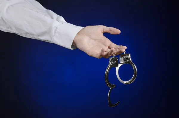 Dishonest and a prison doctor topic: the hand of man in a white shirt with handcuffs on a dark blue background in studio, put handcuffs on the doctor, the illegal sale of organs