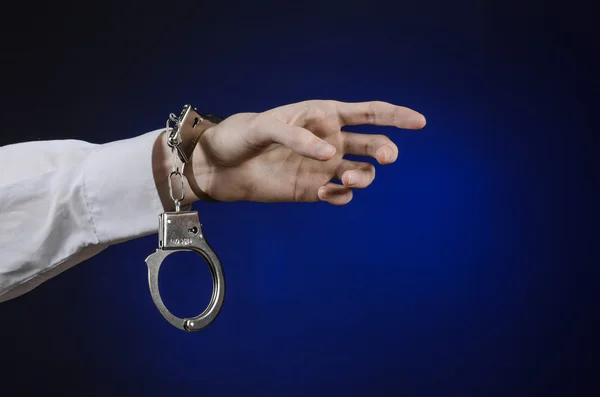Dishonest і тема тюремного лікаря: рука людини в білій сорочці з наручниками на темно-синьому фоні в студії, покласти наручники на лікаря, незаконний продаж органів — стокове фото