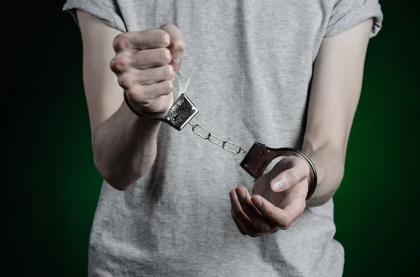 Sujet de prison et condamné : homme menotté sur les mains dans un T-shirt gris et un jean bleu sur un fond vert foncé dans le studio, mettre des menottes sur le dealer de drogue — Photo