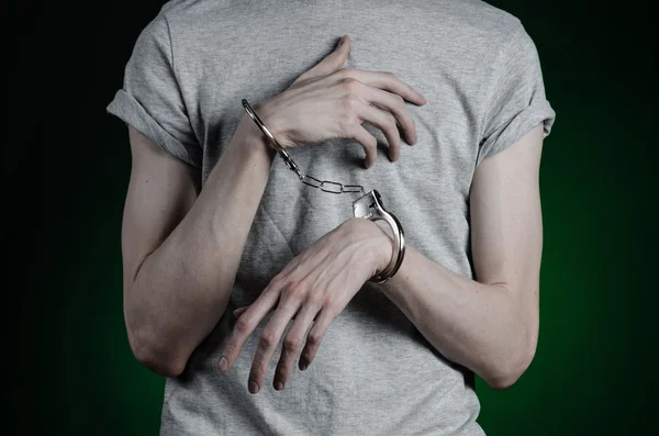 Sujet de prison et condamné : homme menotté sur les mains dans un T-shirt gris et un jean bleu sur un fond vert foncé dans le studio, mettre des menottes sur le dealer de drogue — Photo