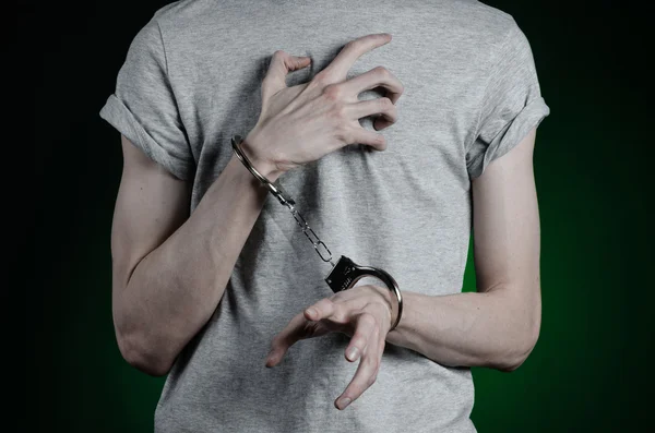 Sujet de prison et condamné : homme menotté sur les mains dans un T-shirt gris et un jean bleu sur un fond vert foncé dans le studio, mettre des menottes sur le dealer de drogue — Photo