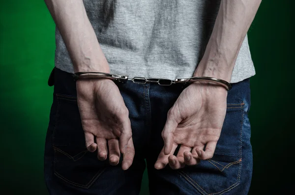 Φυλακή και καταδικάστηκε θέμα: άνθρωπος με χειροπέδες στα χέρια του σε ένα γκρι T-shirt και τζιν μπλε σε σκούρο πράσινο φόντο στο στούντιο, ἐνεδύσατο χειροπέδες εμπόρων ναρκωτικών, η θέα από το πίσω μέρος — Φωτογραφία Αρχείου