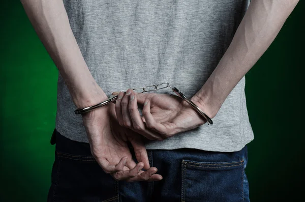 监狱和被定罪的主题: 人与灰色的 t 恤在他手上的手铐和蓝色牛仔裤的暗绿色背景在工作室里，铐上毒贩，从背面视图 — 图库照片