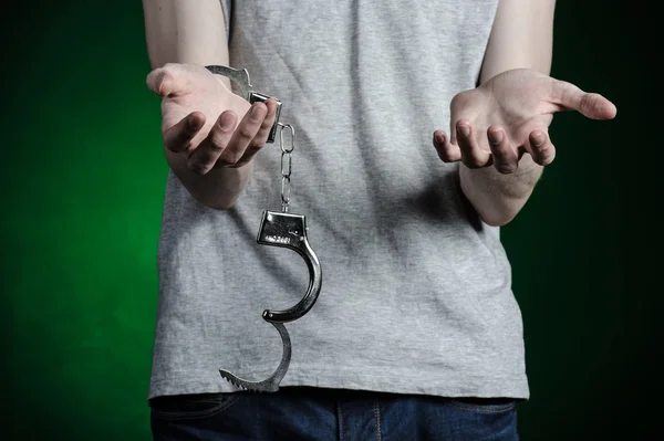 Gefängnis und verurteiltes Thema: Mann mit Handschellen an den Händen in grauem T-Shirt und blauer Jeans auf dunkelgrünem Hintergrund im Studio, legt Drogendealer Handschellen an — Stockfoto