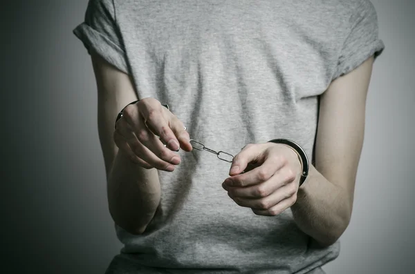 Fängelse och dömda ämne: mannen med handfängsel på händerna i en grå T-shirt på en grå bakgrund i studion, sätta handfängsel på våldtäktsmannen — Stockfoto