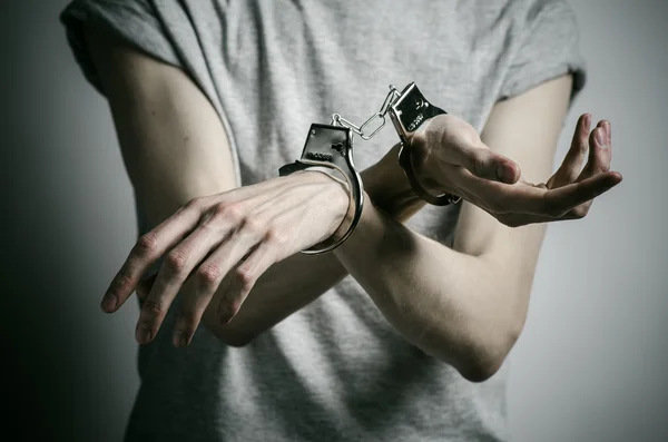 Prisión y tema convicto: hombre con esposas en las manos con una camiseta gris sobre un fondo gris en el estudio, esposado al violador —  Fotos de Stock