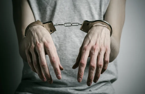 Prigione e argomento condannato: uomo con le manette sulle mani in una maglietta grigia su sfondo grigio in studio, mettere le manette allo stupratore — Foto Stock