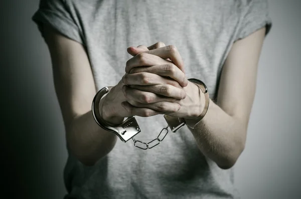 감옥과 유죄 판결된 주제: 강간 범에 수 갑을 넣어 스튜디오에서 회색 배경에 회색 티셔츠에 그의 손에 수 갑을 가진 남자 — 스톡 사진