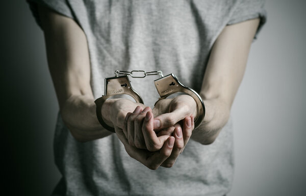 Prison and convicted topic: man with handcuffs on his hands in a gray T-shirt on a gray background in the studio, put handcuffs on rapist
