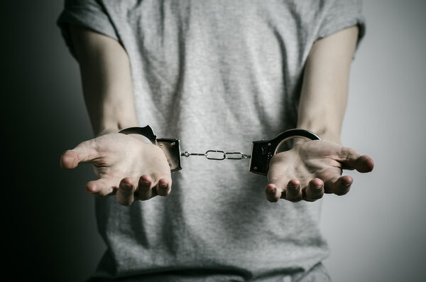 Prison and convicted topic: man with handcuffs on his hands in a gray T-shirt on a gray background in the studio, put handcuffs on rapist