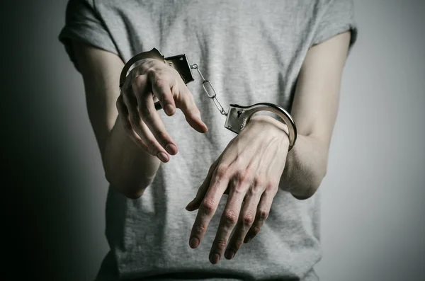 Prison and convicted topic: man with handcuffs on his hands in a gray T-shirt on a gray background in the studio, put handcuffs on rapist