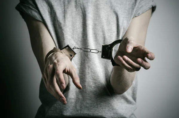 Gevangenis en veroordeelde onderwerp: man met handboeien op zijn handen in een grijs T-shirt op een grijze achtergrond in de studio, handboeien zetten verkrachter — Stockfoto